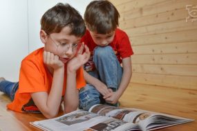 Dwaj chłopcy, w tym jeden w okularach czytający książkę, zdjęcie ilustracyjne